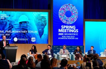 Panel internacional en el Global Parliamentary Forum 2025 durante las Reuniones de Primavera del Banco Mundial y el FMI en Washington D.C. A la izquierda, de pie, un hombre modera el panel desde el podio, mientras seis panelistas debaten frente a una audiencia diversa. Las pantallas LED muestran logotipos del evento y rostros de diferentes personas. Reuniones de primavera