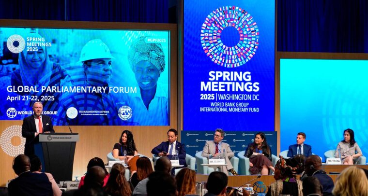 Panel internacional en el Global Parliamentary Forum 2025 durante las Reuniones de Primavera del Banco Mundial y el FMI en Washington D.C. A la izquierda, de pie, un hombre modera el panel desde el podio, mientras seis panelistas debaten frente a una audiencia diversa. Las pantallas LED muestran logotipos del evento y rostros de diferentes personas. Reuniones de primavera
