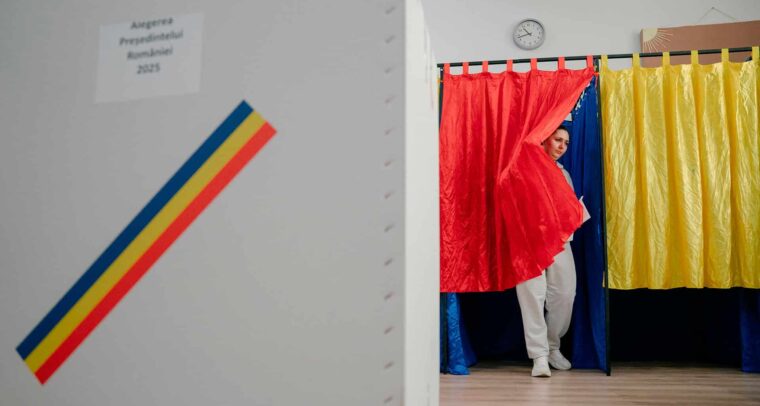 Una votante sale de una cabina de votación decorada con los colores rojo, amarillo y azul de la bandera de Rumanía durante la primera vuelta de las elecciones presidenciales de 2025. Rumanía