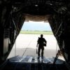 Vista desde el interior de una aeronave militar de transporte, con un soldado descendiendo por la rampa trasera hacia la pista de aterrizaje en un día soleado. UE