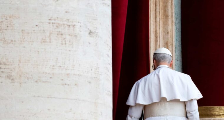Pope Leo IV, seen from behind and dressed in the papal cassock, walked away after delivering his first Regina Caeli prayer from a balcony overlooking St. Peter’s Square. On the left, part of the building clad in light travertine can be seen, while a column of the same stone, framed by red curtains, stands behind him. Pope