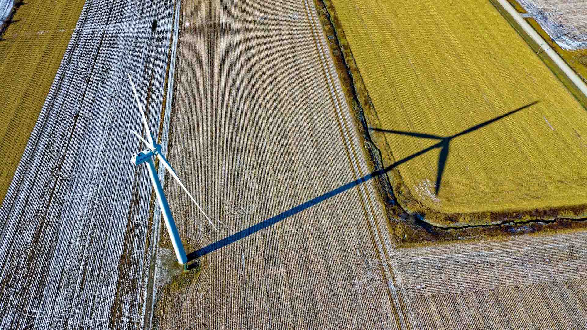 Vista aérea de una turbina eólica proyectando sombra sobre campos agrícolas parcialmente cubiertos de nieve en el Dodge Center de Minnesota (Estados Unidos). Trump