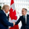Donald Trump (de pie, con traje azul marino, corbata roja y camisa blanca) saluda con un apretón de manos a Mark Carney (también de pie, con traje y corbata azul marino y camisa blanca) en la entrada del Ala Oeste de la Casa Blanca, el 6 de mayo de 2025. En el centro de la imagen se aprecia una bandera de Canadá entre ambos. Al fondo se distingue parte del edificio y, a la derecha, un coche negro. Canadá