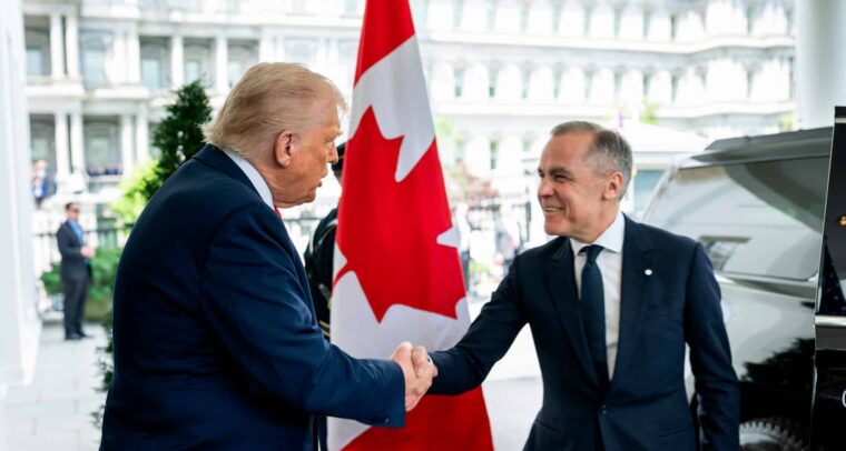 Donald Trump (de pie, con traje azul marino, corbata roja y camisa blanca) saluda con un apretón de manos a Mark Carney (también de pie, con traje y corbata azul marino y camisa blanca) en la entrada del Ala Oeste de la Casa Blanca, el 6 de mayo de 2025. En el centro de la imagen se aprecia una bandera de Canadá entre ambos. Al fondo se distingue parte del edificio y, a la derecha, un coche negro. Canadá