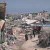 Zona urbana devastada en Gaza con escombros, edificios colapsados y personas caminando entre las ruinas. Gaza