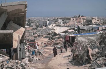 Zona urbana devastada en Gaza con escombros, edificios colapsados y personas caminando entre las ruinas. Gaza