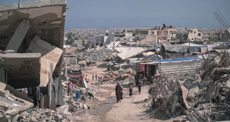 Zona urbana devastada en Gaza con escombros, edificios colapsados y personas caminando entre las ruinas. Gaza