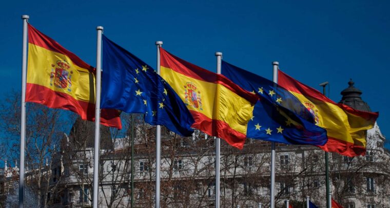 Banderas de España y de la Unión Europea ondeando en la plaza de Cánovas del Castillo (Plaza de Neptuno) en Madrid. Tras los árboles, el edificio del Hotel Ritz. Foto: acho Arenas (CC BY-NC-SA 2.0).