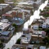 Vista aérea diurna de un vecindario urbano en Piura (Perú), afectado por inundaciones tras el paso de 'El Niño Costero' en 2017. Las calles están cubiertas de agua y algunas personas caminan por zonas anegadas. Las viviendas de varios pisos muestran daños visibles, mientras el nivel del agua permanece alto. América Latina