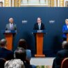 De izquierda a derecha, António Costa (con traje gris, camisa azul clara y corbata lila), presidente del Consejo Europeo; Keir Starmer (con traje negro, camisa blanca y corbata azul), primer ministro del Reino Unido; y Ursula von der Leyen (con chaqueta azul, camisa blanca y pantalones negros), presidenta de la Comisión Europea, de pie detrás de atriles con el rótulo "UK-EU Summit 2025", durante una rueda de prensa conjunta celebrada el 19 de mayo de 2025 en una sala con ornamentación dorada, pinturas clásicas y banderas de la UE y del Reino Unido al fondo. Frente a ellos, un grupo de personas los escucha con atención. Reino Unido