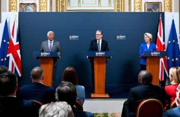 De izquierda a derecha, António Costa (con traje gris, camisa azul clara y corbata lila), presidente del Consejo Europeo; Keir Starmer (con traje negro, camisa blanca y corbata azul), primer ministro del Reino Unido; y Ursula von der Leyen (con chaqueta azul, camisa blanca y pantalones negros), presidenta de la Comisión Europea, de pie detrás de atriles con el rótulo "UK-EU Summit 2025", durante una rueda de prensa conjunta celebrada el 19 de mayo de 2025 en una sala con ornamentación dorada, pinturas clásicas y banderas de la UE y del Reino Unido al fondo. Frente a ellos, un grupo de personas los escucha con atención. Reino Unido