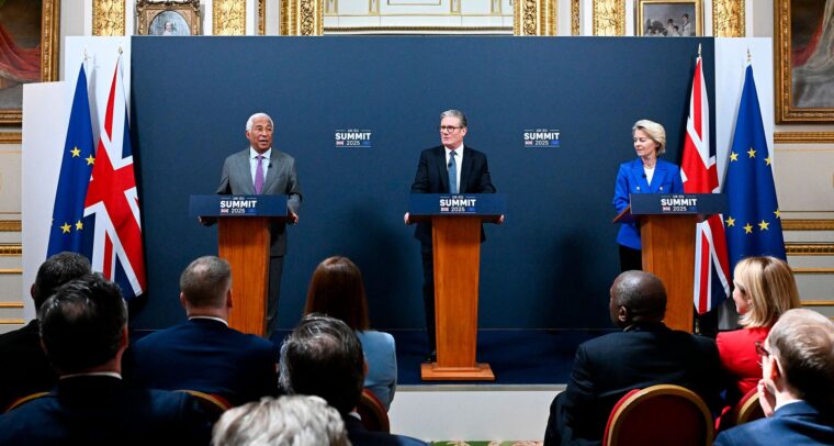 De izquierda a derecha, António Costa (con traje gris, camisa azul clara y corbata lila), presidente del Consejo Europeo; Keir Starmer (con traje negro, camisa blanca y corbata azul), primer ministro del Reino Unido; y Ursula von der Leyen (con chaqueta azul, camisa blanca y pantalones negros), presidenta de la Comisión Europea, de pie detrás de atriles con el rótulo "UK-EU Summit 2025", durante una rueda de prensa conjunta celebrada el 19 de mayo de 2025 en una sala con ornamentación dorada, pinturas clásicas y banderas de la UE y del Reino Unido al fondo. Frente a ellos, un grupo de personas los escucha con atención. Reino Unido