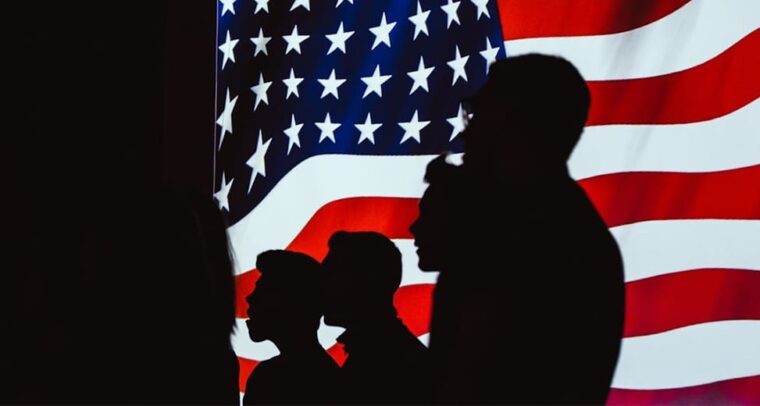 Siluetas humanas delante de una bandera de Estados Unidos en una pantalla iluminada. Estados Unidos
