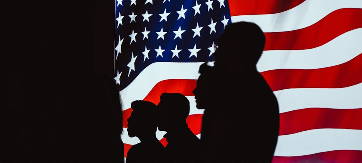 Siluetas humanas delante de una bandera de Estados Unidos en una pantalla iluminada. Estados Unidos