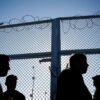 Siluetas de varias personas migrantes que esperan frente a una valla con alambre de espino en un centro de registro de un campo de refugiados en Lesbos (Grecia), en un día soleado. Migración