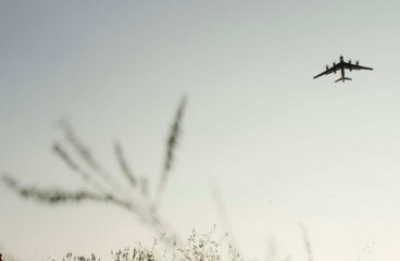 Silueta de un avión militar Tu-95 regresando a su base, volando a baja altura sobre un campo con vegetación al atardecer. A la izquierda, se distingue la silueta de una persona con una mochila. Ucrania