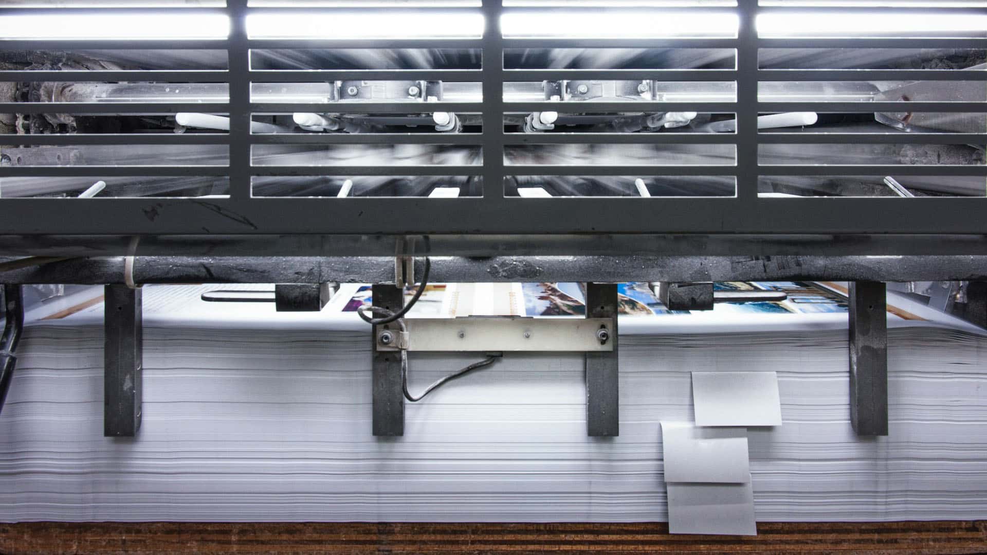 Máquina de impresión industrial imprimiendo hojas a color sobre una pila de papel blanco. España