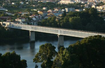 Puente internacional de estructura metálica con diseño de celosía, apoyado sobre pilares de hormigón, que cruza el río Miño conectando las localidades de Tuy (España) y Valença do Minho (Portugal), rodeado de paisaje urbano y vegetación. Europa