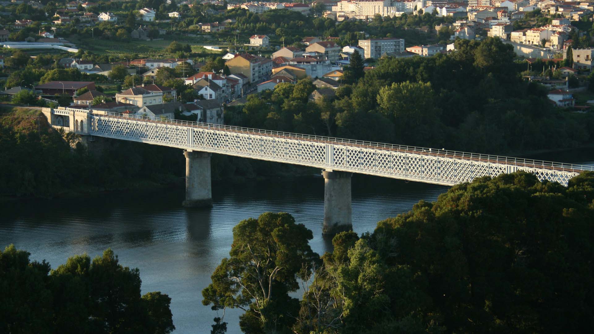 Puente internacional de estructura metálica con diseño de celosía, apoyado sobre pilares de hormigón, que cruza el río Miño conectando las localidades de Tuy (España) y Valença do Minho (Portugal), rodeado de paisaje urbano y vegetación. Europa