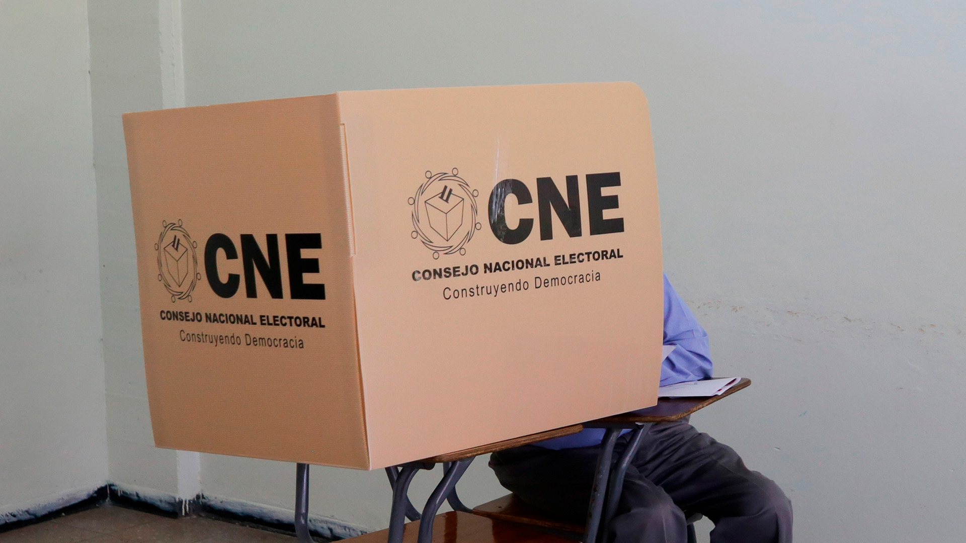 Un ciudadano hondureño (sentado, con pantalones grises y camisa azul) emite su voto en un centro electoral de Tegucigalpa durante las elecciones primarias, dentro de una cabina del Consejo Nacional Electoral (CNE), 9 de marzo de 2025. electoral