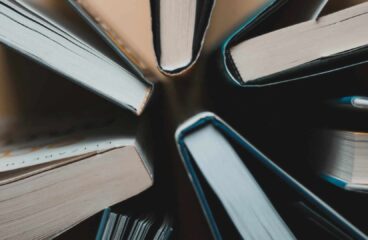 Vista cenital de varios libros abiertos, dispuestos en círculo, mostrando los cantos de las páginas y las cubiertas. Libros