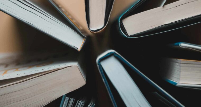 Vista cenital de varios libros abiertos, dispuestos en círculo, mostrando los cantos de las páginas y las cubiertas. Libros