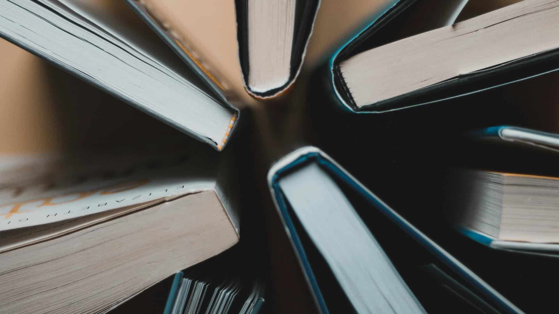 Vista cenital de varios libros abiertos, dispuestos en círculo, mostrando los cantos de las páginas y las cubiertas. Libros