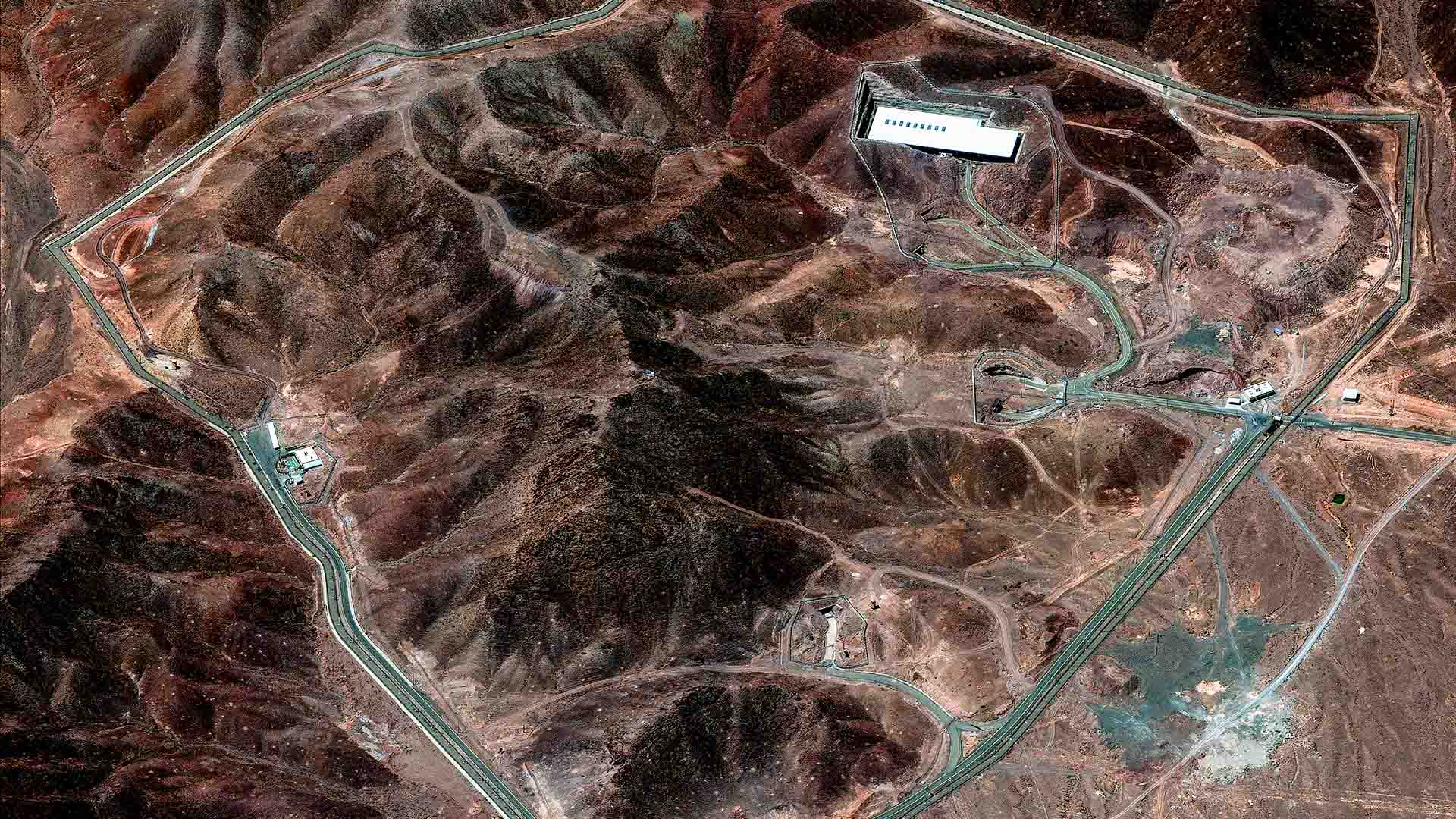 Vista satelital de la instalación de enriquecimiento de Fordo, tomada el 14 de junio de 2025. El complejo, ubicado en una zona montañosa, está rodeado por una carretera perimetral. En la parte superior de la imagen se distingue el techo blanco de un edificio. Irán