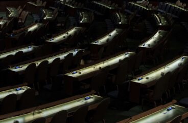 Salón de la Asamblea General de Naciones Unidas después de una reunión, sin delegados presentes, con la única iluminación procedente de los escritorios dispuestos en forma circular. ONU