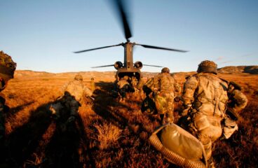 Spanish Army soldiers running towards a helicopter with its rotor blades spinning, during a field training exercise. Defence