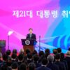 Ceremonia de investidura de Lee Jae-myung, como presidente número 21 de Corea del Sur en la Asamblea Nacional de Seúl, el 4 de junio de 2025. Lee está de pie en el podio presidencial, con traje oscuro y corbata azul, dirigiéndose a la audiencia. Al fondo, una pantalla rosa muestra el texto 'La ceremonia de investidura del 21.º presidente' en coreano, junto a banderas nacionales. Lee Jae-myung