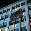 Bandera de la Unión Europea ondea frente a un edificio institucional iluminado con las estrellas de la UE en Berlín (Alemania), durante la noche. Generación Europa