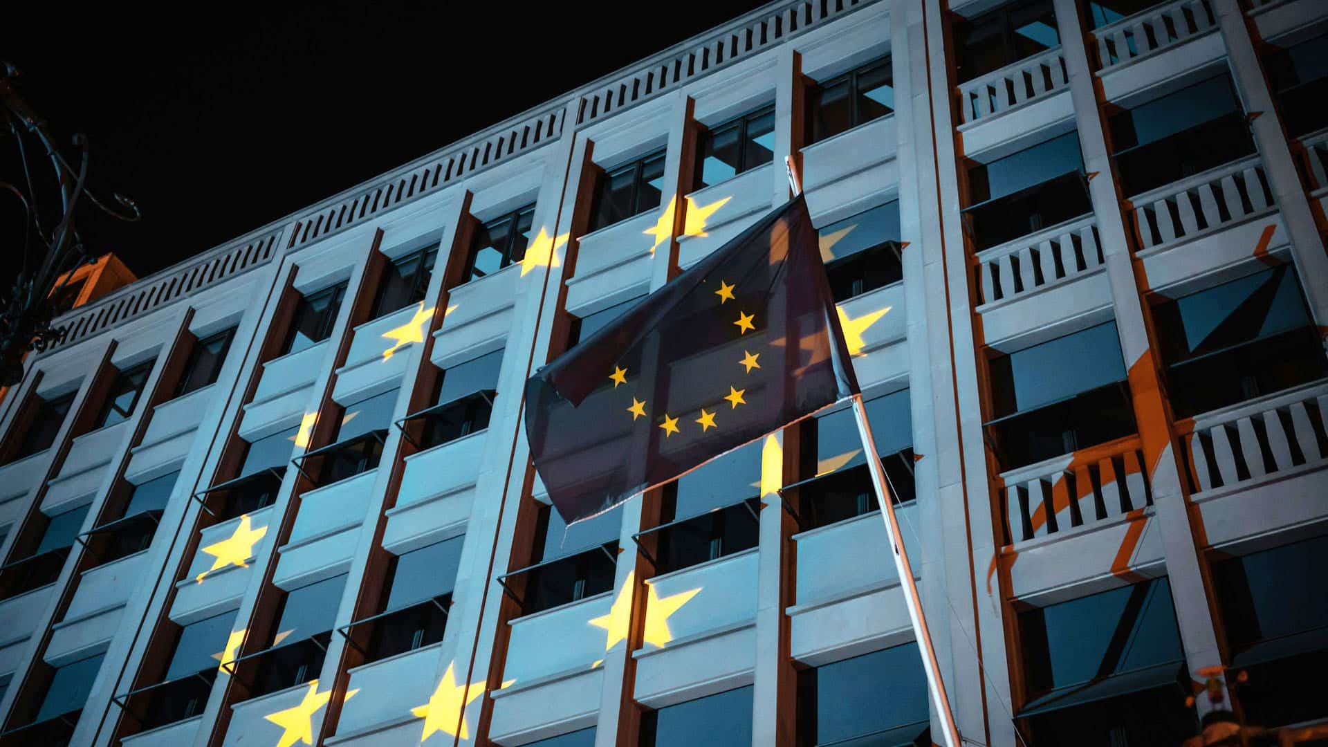 Bandera de la Unión Europea ondea frente a un edificio institucional iluminado con las estrellas de la UE en Berlín (Alemania), durante la noche. Generación Europa