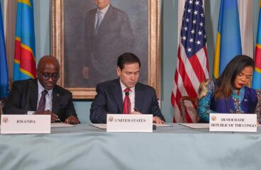 Marco Rubio, la ministra de Asuntos Exteriores de la República Democrática del Congo, Thérèse Kayikwamba Wagner, y el ministro de Asuntos Exteriores de Ruanda, Olivier Nduhungirehe, sentados firmando el Acuerdo de Paz en el Departamento de Estado en Washington D.C., el 27 de junio de 2025. Frente a ellos, una mesa con los nombres de los tres países y banderas de la República Democrática del Congo, Ruanda y Estados Unidos a ambos lados. Acuerdo