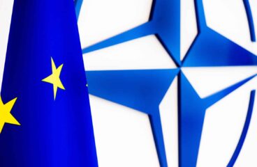 Bandera de la Unión Europea delante del emblema de la OTAN en una pared blanca. OTAN