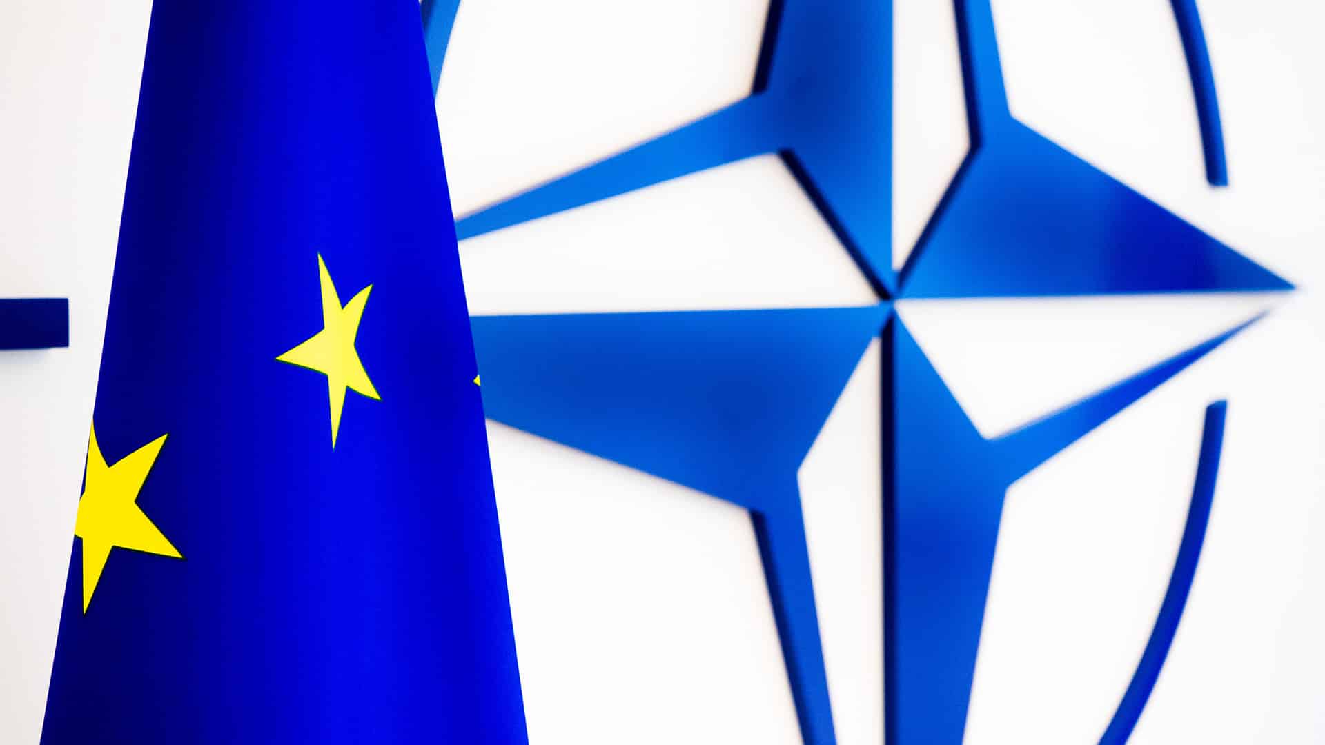 Bandera de la Unión Europea delante del emblema de la OTAN en una pared blanca. OTAN