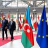 De izquierda a derecha: Ilham Aliyev (presidente de Azerbaiyán), Charles Michel (presidente del Consejo Europeo en 2023) y Nikol Pashinián (primer ministro de Armenia) caminan por la alfombra roja rodeada de banderas en la entrada de la sede del Consejo Europeo, para la reunión con los mandatarios de Francia y Alemania (1/06/2023), tras los enfrentamientos entre Azerbaiyán y Armenia en la región de Nagorno Karabaj. Se destacan las banderas de Azerbaiyán, la UE y Armenia en primer plano.