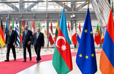 De izquierda a derecha: Ilham Aliyev (presidente de Azerbaiyán), Charles Michel (presidente del Consejo Europeo en 2023) y Nikol Pashinián (primer ministro de Armenia) caminan por la alfombra roja rodeada de banderas en la entrada de la sede del Consejo Europeo, para la reunión con los mandatarios de Francia y Alemania (1/06/2023), tras los enfrentamientos entre Azerbaiyán y Armenia en la región de Nagorno Karabaj. Se destacan las banderas de Azerbaiyán, la UE y Armenia en primer plano.