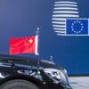 Parte frontal de un coche negro de lujo con una bandera de China en miniatura, frente a un fondo azul con el logo del Consejo Europeo. La foto es de la Cumbre China-UE de 2017 en Bruselas (Bélgica).