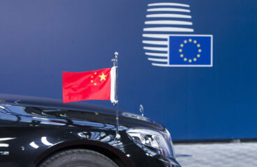 Front of a black luxury car with a miniature Chinese flag in front of a blue background with the logo of the European Council. The photo is from the 2017 China-EU Summit in Brussels, Belgium.
