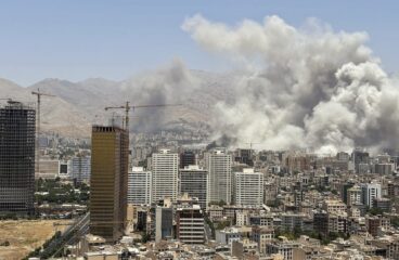 Vista de Tehrán con grandes columnas de humo tras varios edificios altos y grúas de construcción con montañas al fondo, tras un ataque aéreo israelí el 24 de junio de 2025, como parte de la guerra Israel-Irán.