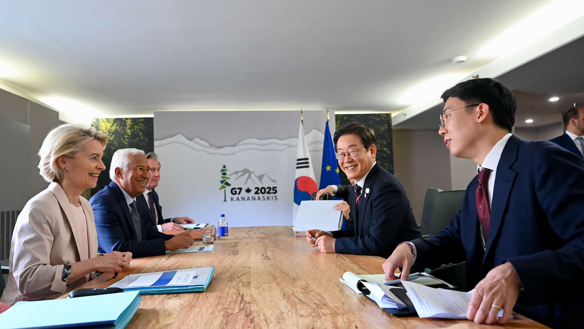 Six people in formal attire sit around a wooden table in a conference room at the G7 Summit in Canada on 17 June 2025. In the background, a sign with the text “G7 + 2025 Kananaskis” and the flags of the Republic of Korea and the European Union. Among those attending the meeting: Lee-Jae Myung (President of the Republic of Korea, second on the right), Ursula von der Leyen (President of the European Commission, first on the left) and Antonio Costa (President of the European Council, second on the left).