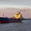 El petrolero Varzuga navega al atardecer por el río Dviná Septentrional en Arcángel (Rusia). A la izquierda se ve una iglesia ortodoxa con cúpulas doradas y al fondo un puente cruza el río. Flota fantasma