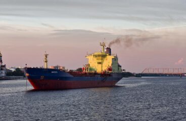 El petrolero Varzuga navega al atardecer por el río Dviná Septentrional en Arcángel (Rusia). A la izquierda se ve una iglesia ortodoxa con cúpulas doradas y al fondo un puente cruza el río. Flota fantasma