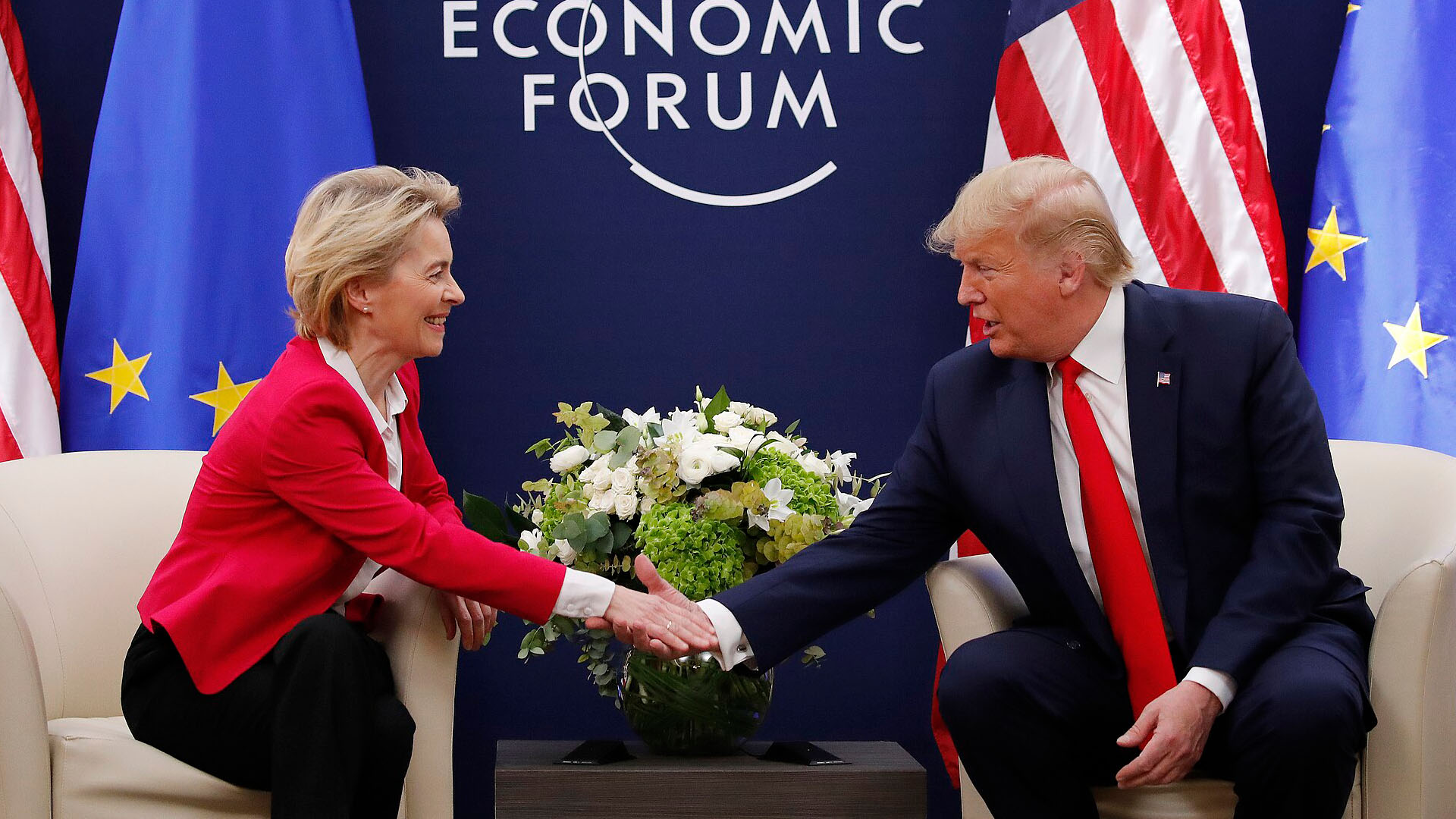 Ursula von der Leyen (presidenta de la Comisión Europea) y Donald Trump (presidente de EEUU) estrechan manos en el Foro Económico Mundial de Davos 2020 durante una reunión bilateral entre la Unión Europea y Estados Unidos, con banderas de ambos bloques al fondo. Acuerdo comercial
