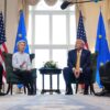 Ursula von der Leyen (presidenta de la Comisión Europea) y Donald Trump (presidente de EEUU) conversan frenta a frente con una mesa y arreglo floral entre ellos durante el encuentro bilateral en Turnberry (Escocia), el 27 de julio de 2025, acompañados por sus delegaciones a los lados y con banderas oficiales de la UE y EEUU al fondo.