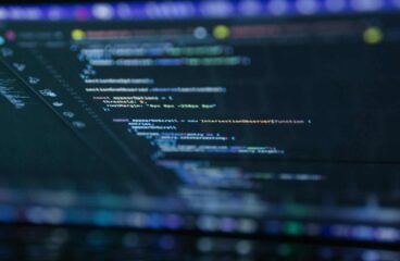 Lines of code on a laptop screen with text highlighted in orange, blue, white, and green on a dark background. Open source