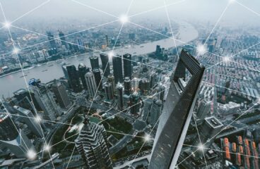 Vista aérea de Shanghái con rascacielos y el río que la atraviesa, sobrepuesta con una red de líneas blancas y puntos brillantes que simbolizan la conectividad digital.