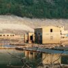Ruinas del pueblo de Aceredo (provincia de Galicia), con casas abandonadas, agua en primer plano y montañas arboladas al fondo. El pueblo ha emergido tras la sequía del embalse de Lindoso en la frontera entre España y Portugal (península Ibérica).