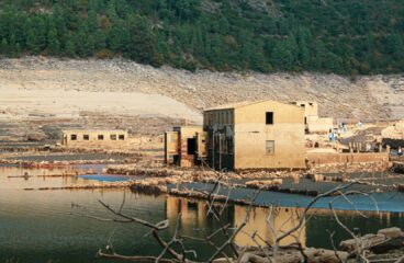Ruinas del pueblo de Aceredo (provincia de Galicia), con casas abandonadas, agua en primer plano y montañas arboladas al fondo. El pueblo ha emergido tras la sequía del embalse de Lindoso en la frontera entre España y Portugal (península Ibérica).